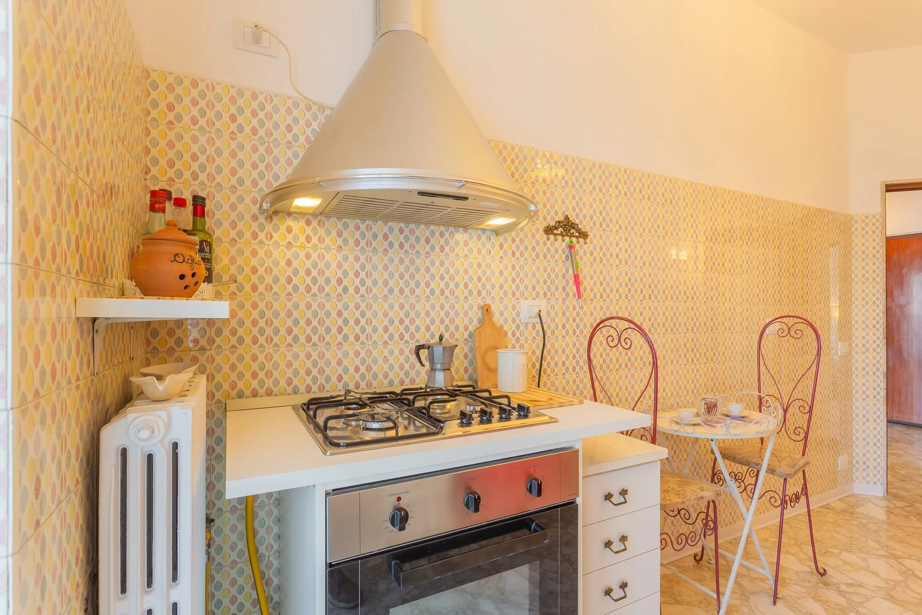 A tiled kitchen with a gas cooktop, range hood, and small dining table.