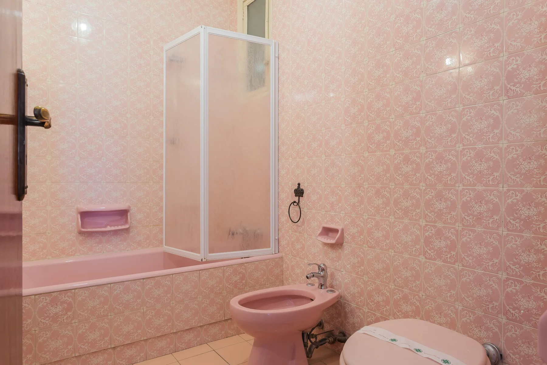 A bathroom with a shower, toilet, and pink patterned wall tiles.