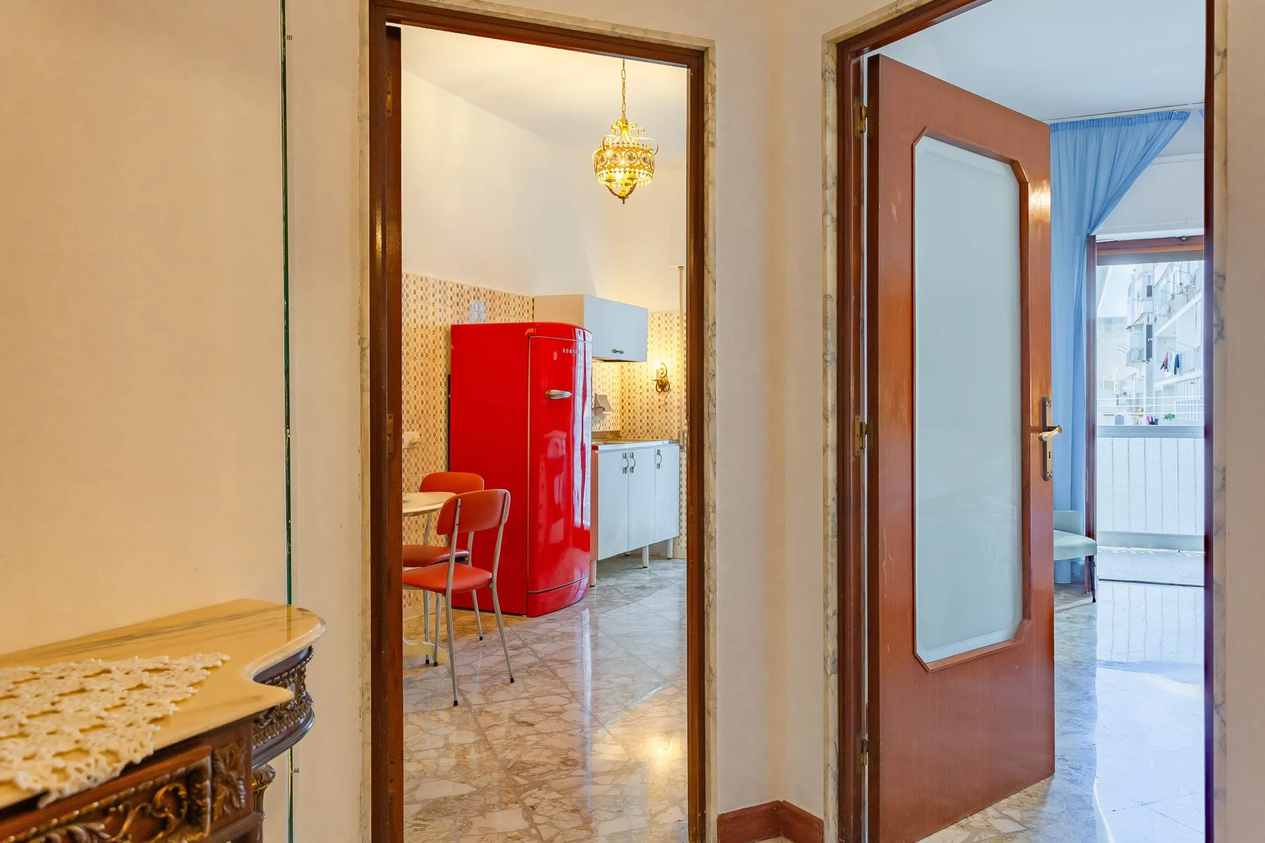 A tiled kitchen with a red refrigerator is visible through the doorway.