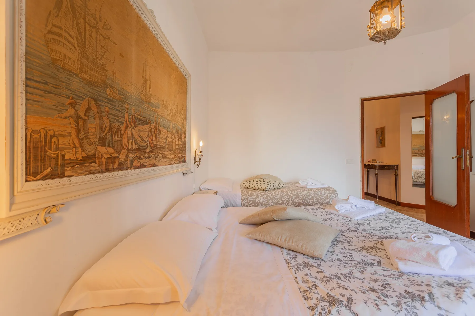 A bedroom with a bed and a large framed wall tapestry.