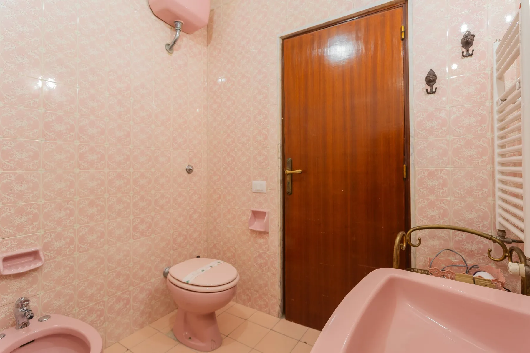 A pink-tiled bathroom with a bathtub, toilet, and wooden door.