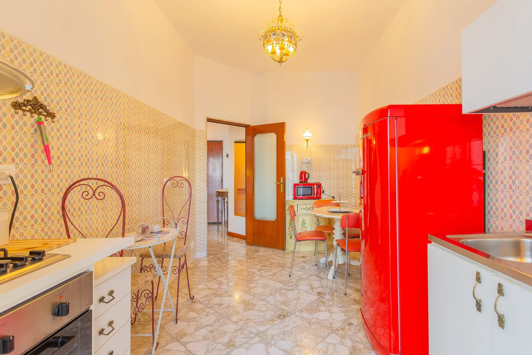 A bright kitchen with patterned walls, a dining table, and a red refrigerator.