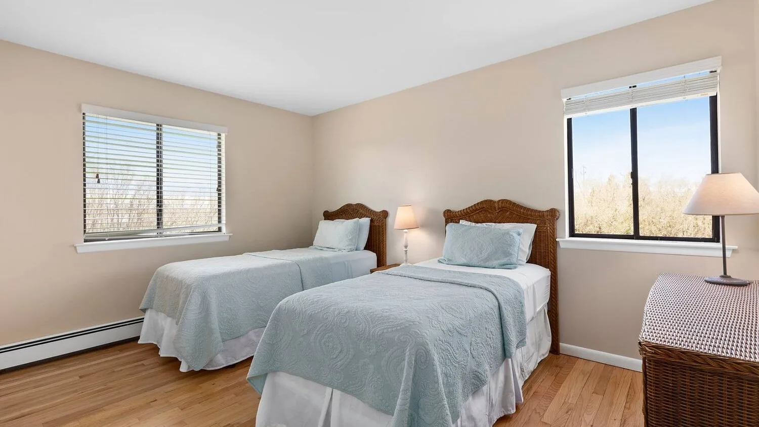 A bedroom with two beds and windows overlooking trees.