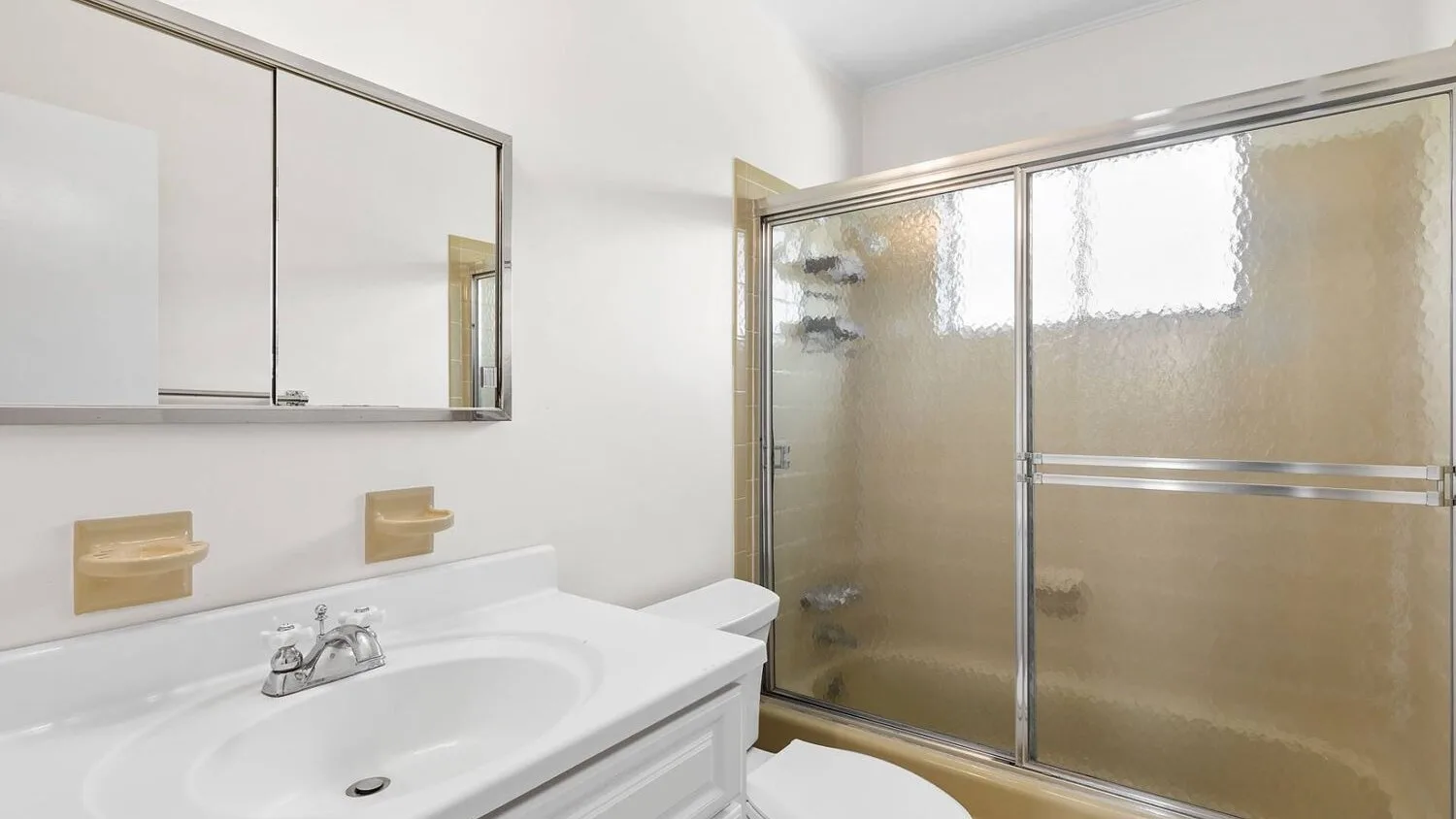 A bright bathroom with a sink and a frosted-glass shower.