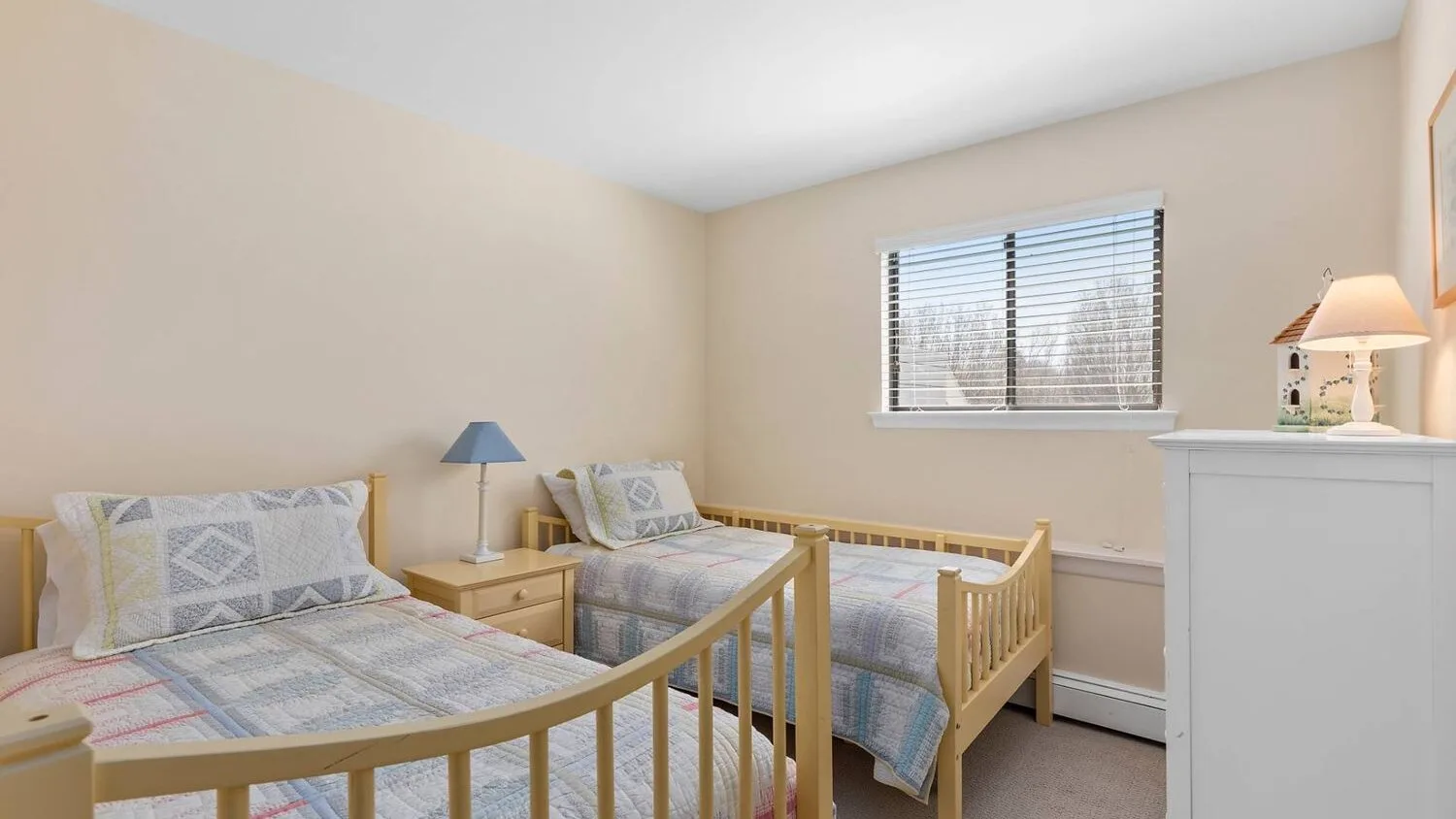 A bedroom with two single beds, a window, and a bedside table.