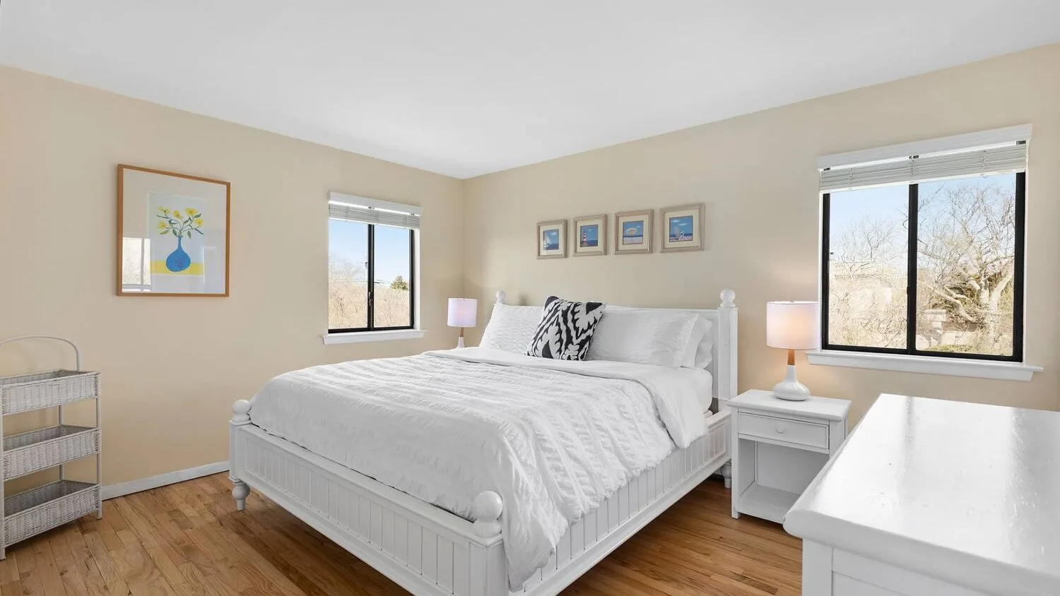 A bright bedroom with a white bed, bedside tables, and large windows.