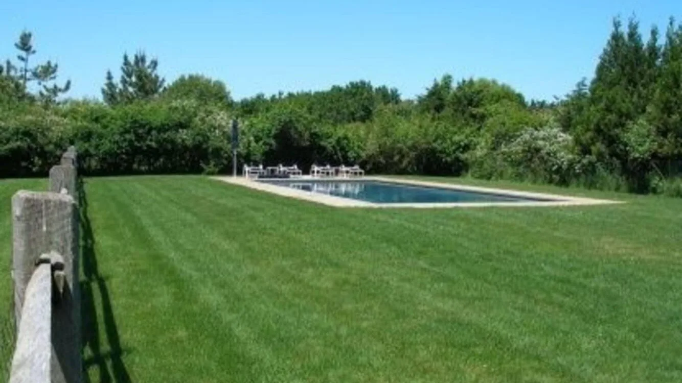 A grassy lawn leads to an outdoor swimming pool bordered by trees.
