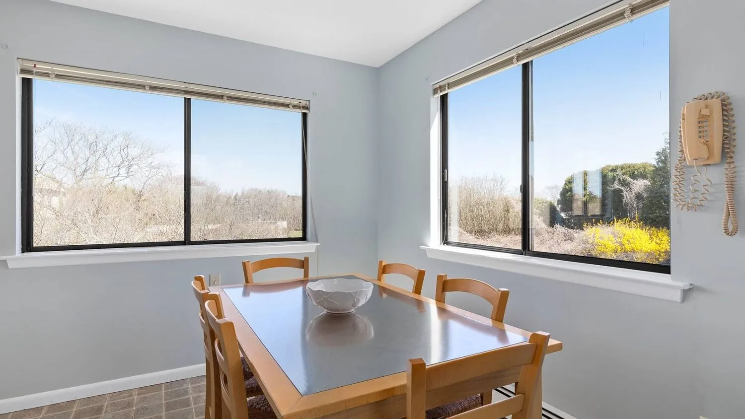 A dining area with a wooden table beside two large windows.