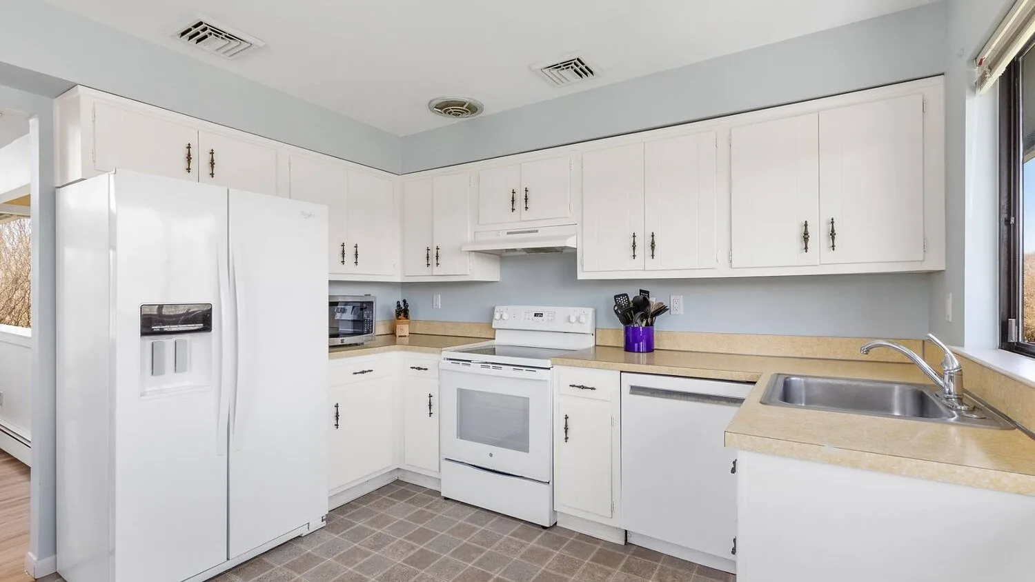 A bright kitchen with white cabinets, a refrigerator, and a sink.