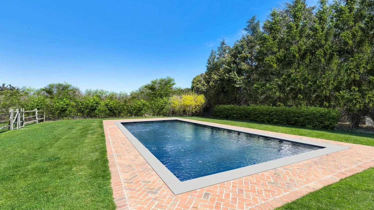 An outdoor swimming pool sits in a brick patio surrounded by lawn and trees.