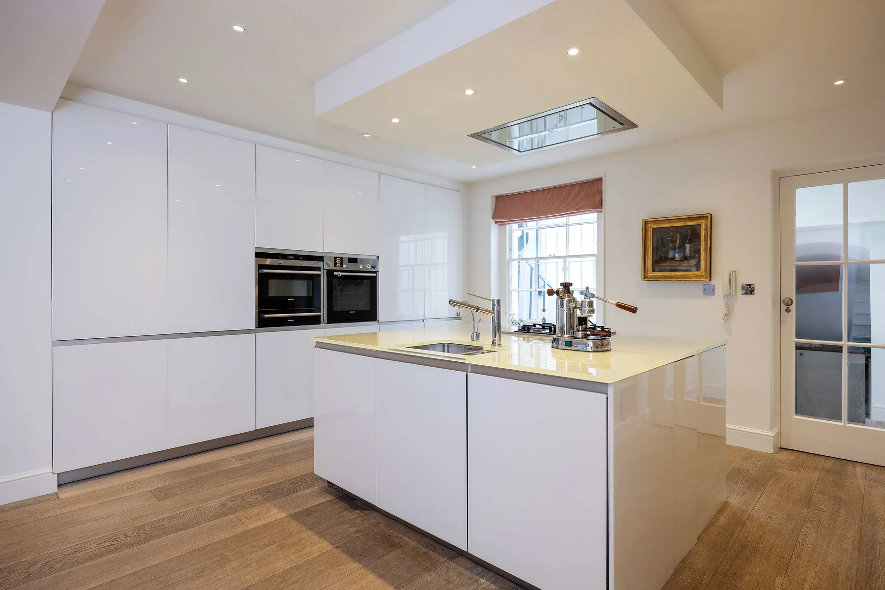 Una cocina moderna y luminosa con gabinetes blancos, una isla central y ventanas grandes.