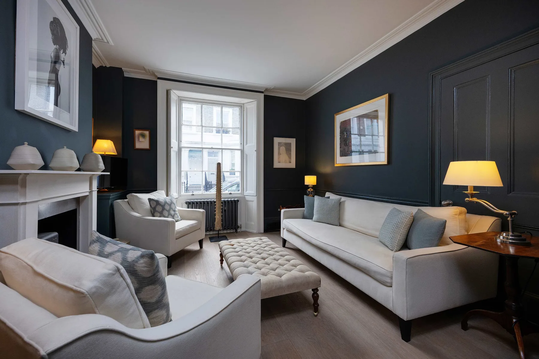A sitting room with pale seating, framed artwork, and a fireplace.