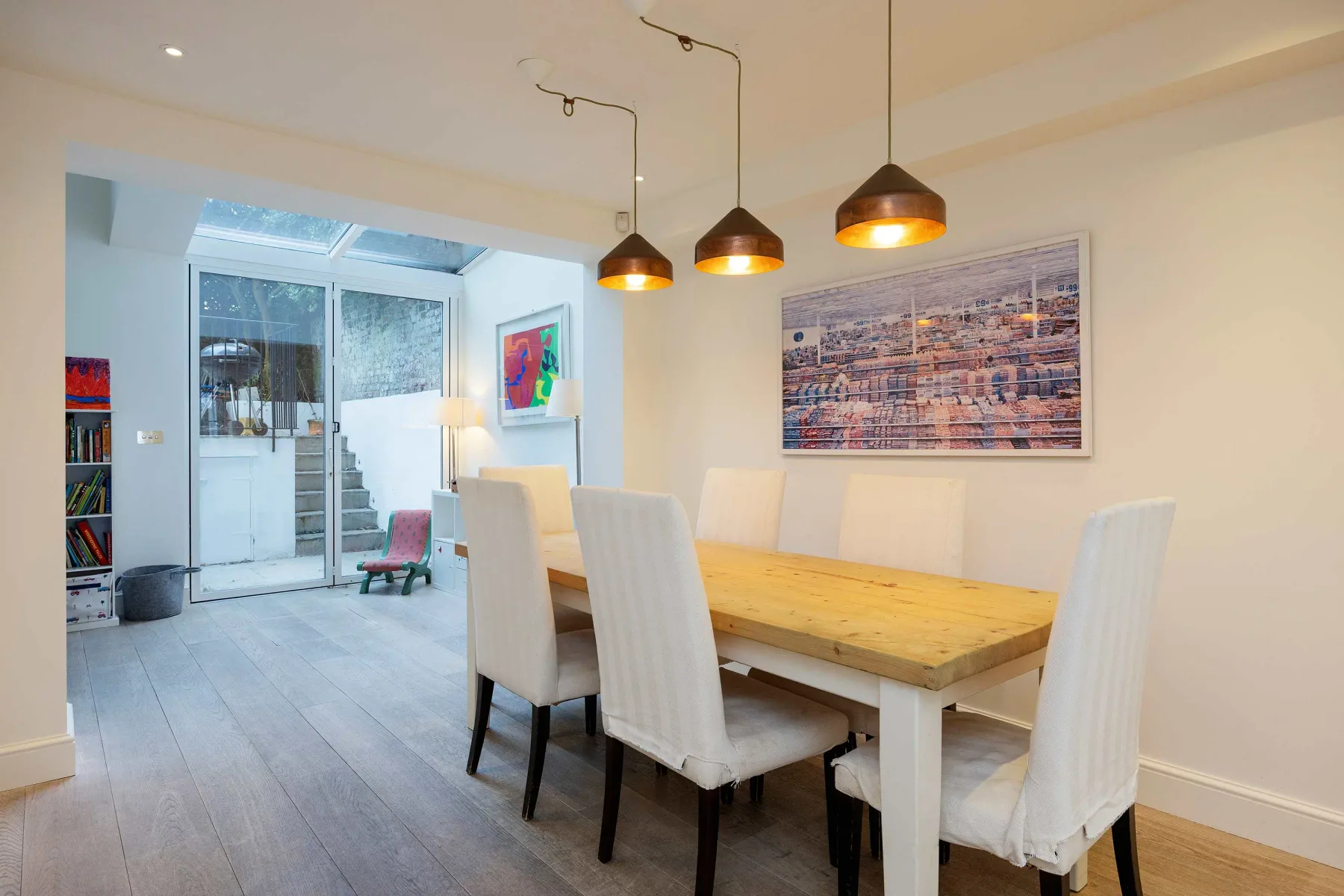 Un comedor con una mesa de madera y asientos blancos bajo lámparas colgantes.