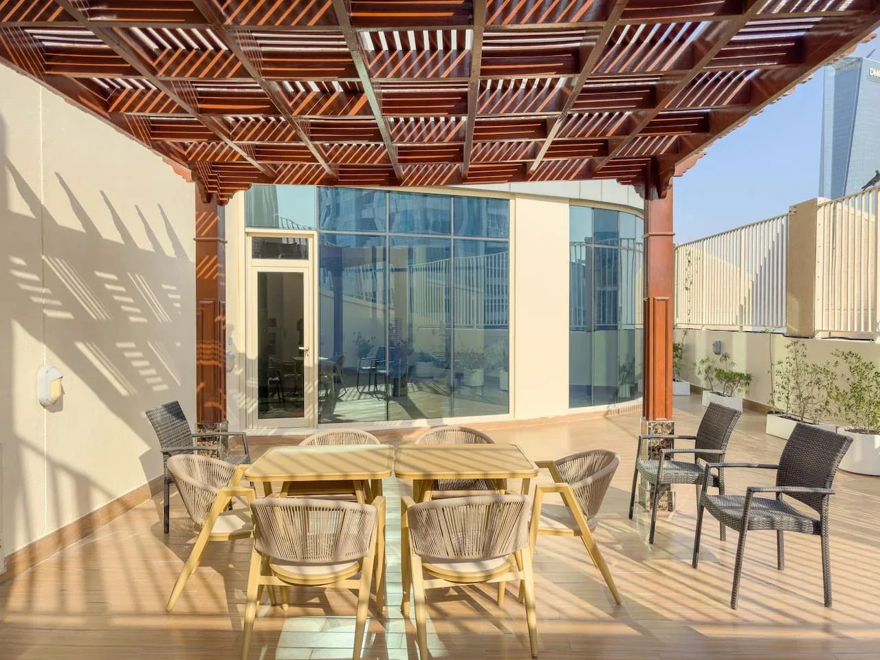 Comedor al aire libre bajo una pérgola de madera, con mesa y asientos.
