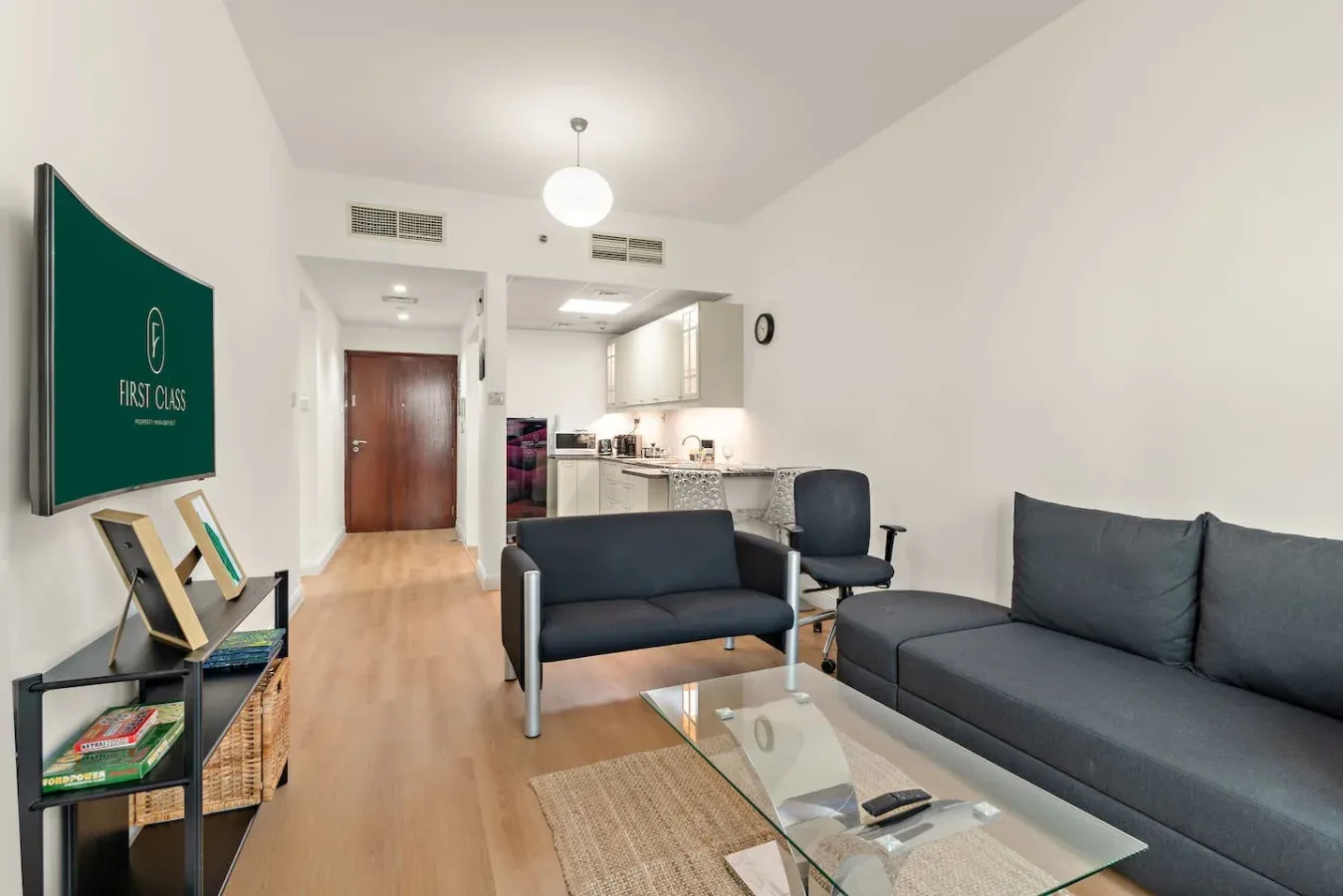 Una sala de estar con asientos y una mesa de centro de vidrio se abre a una cocina.