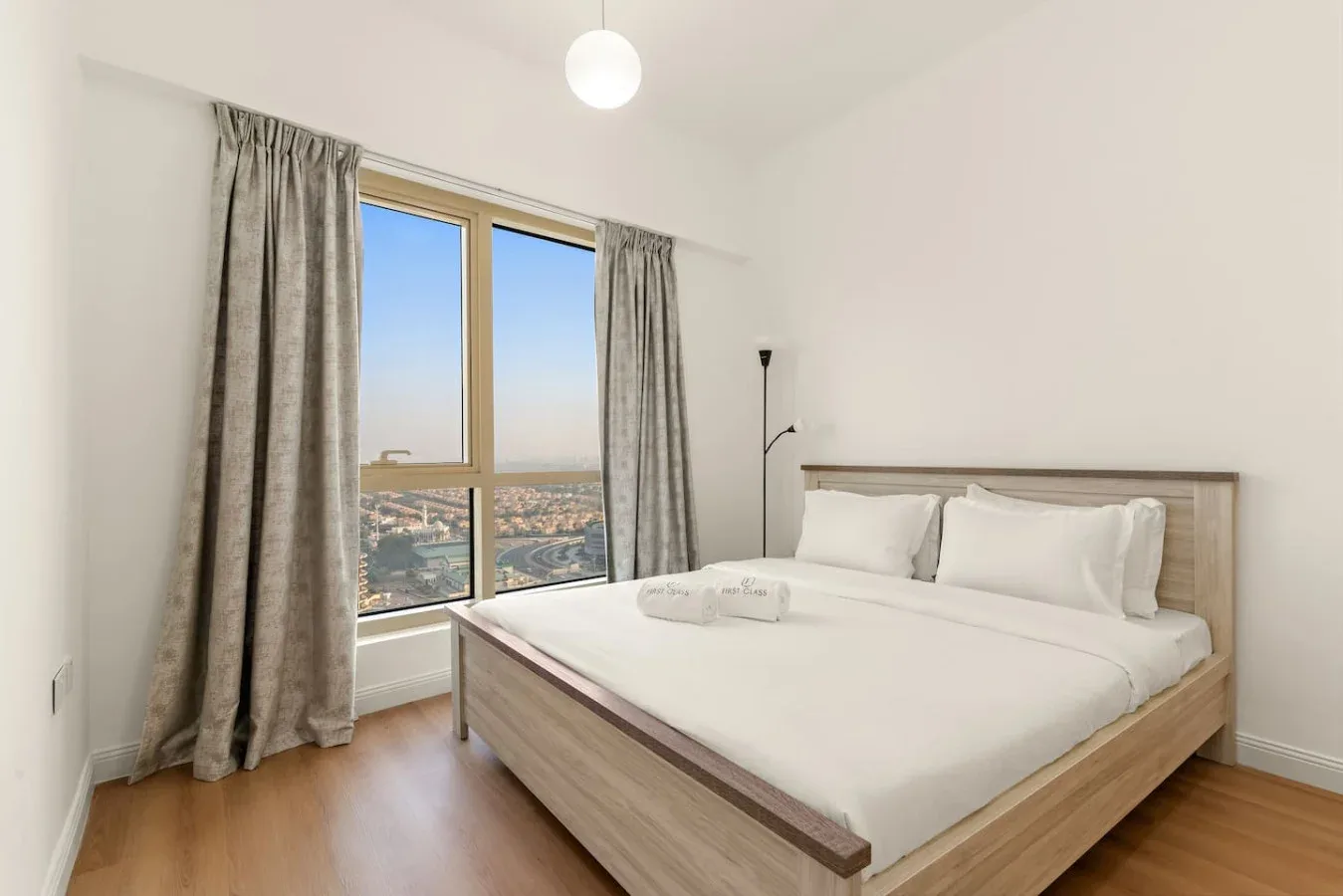 Un dormitorio luminoso con una cama bien tendida junto a una ventana grande.