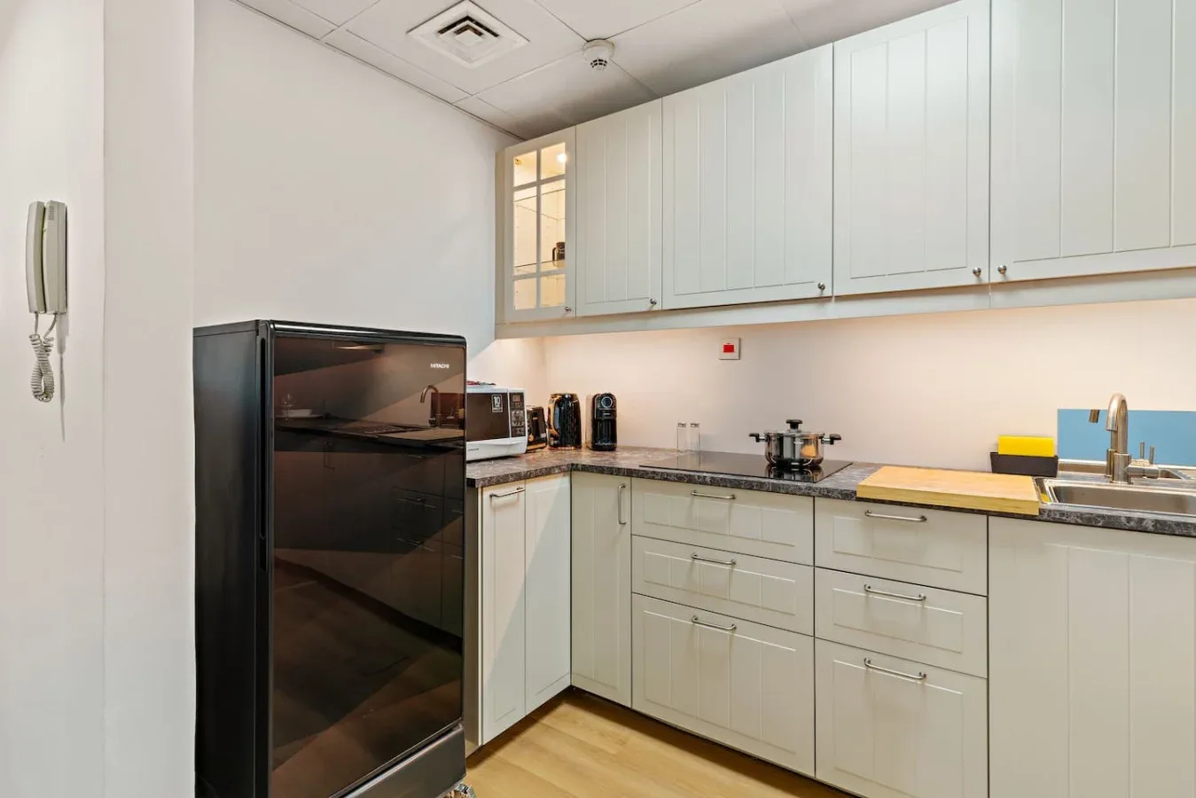 Una cocina luminosa con gabinetes blancos, un refrigerador oscuro y una encimera.