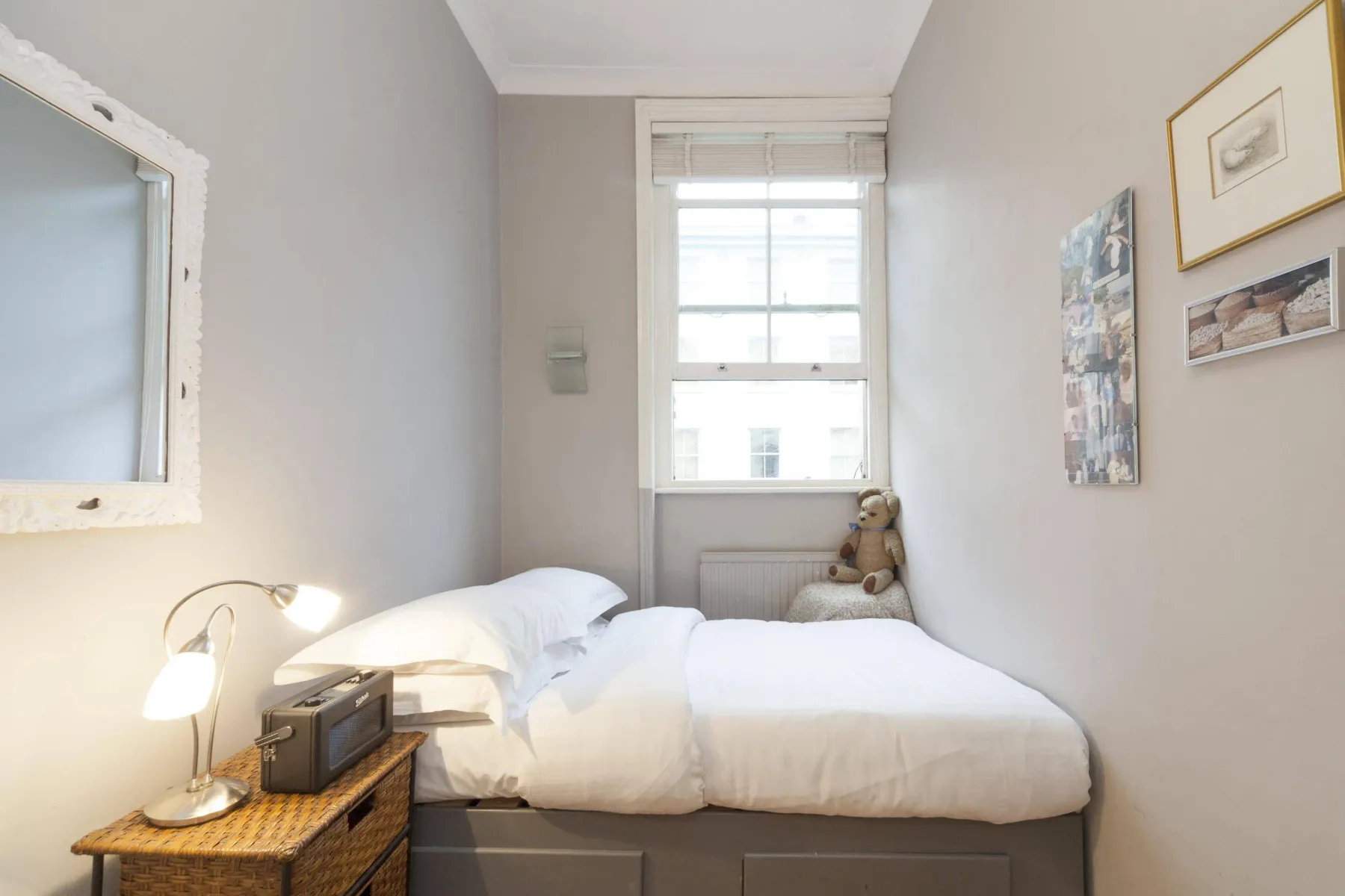 A bedroom with a bed beneath a window and framed pictures on the wall.