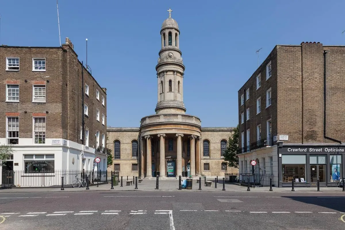 A columned church entrance and tower stand between brick buildings along a city street.
