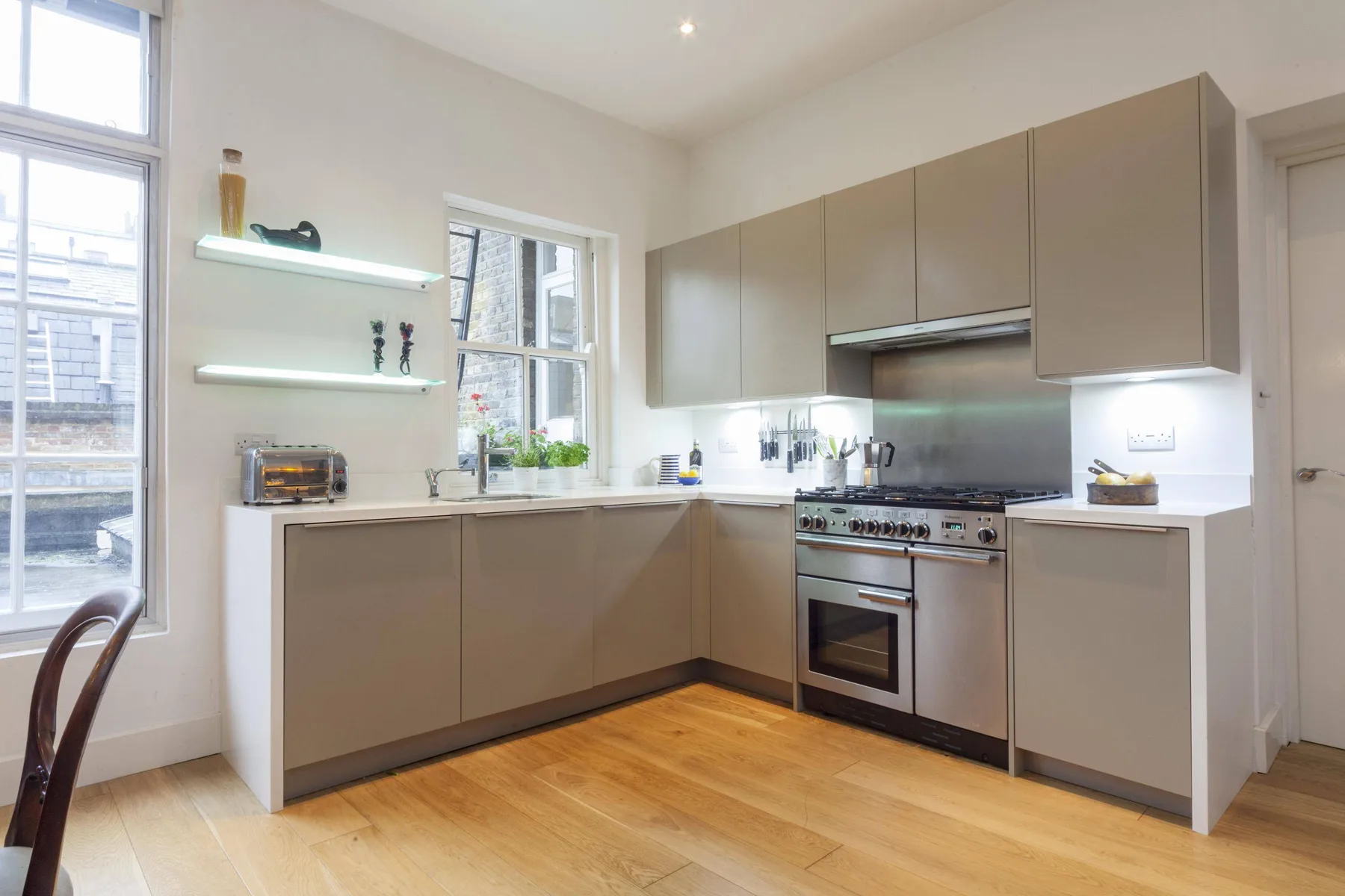A modern kitchen with taupe cabinets, stainless steel appliances, and wooden flooring.