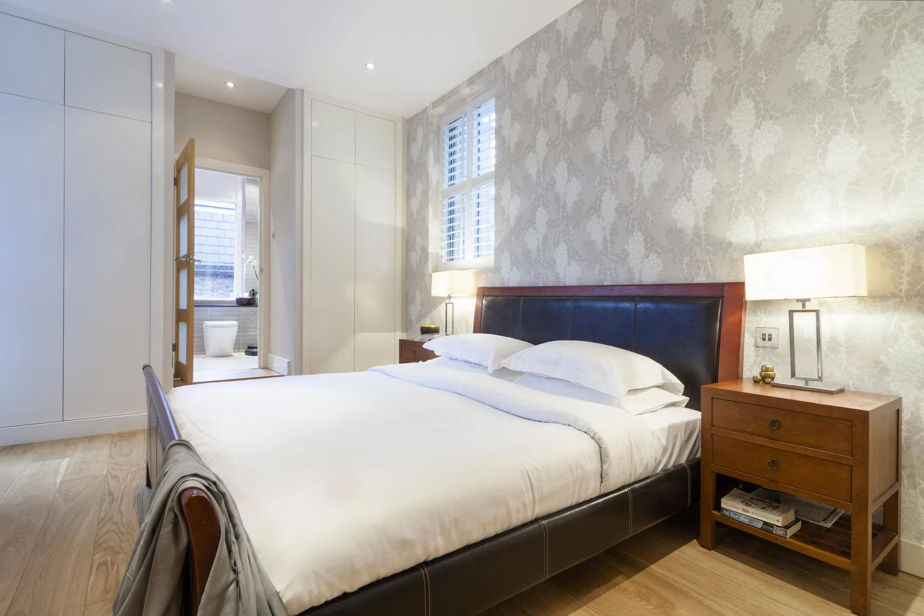 A bedroom with a neatly made bed, bedside tables, and a window.