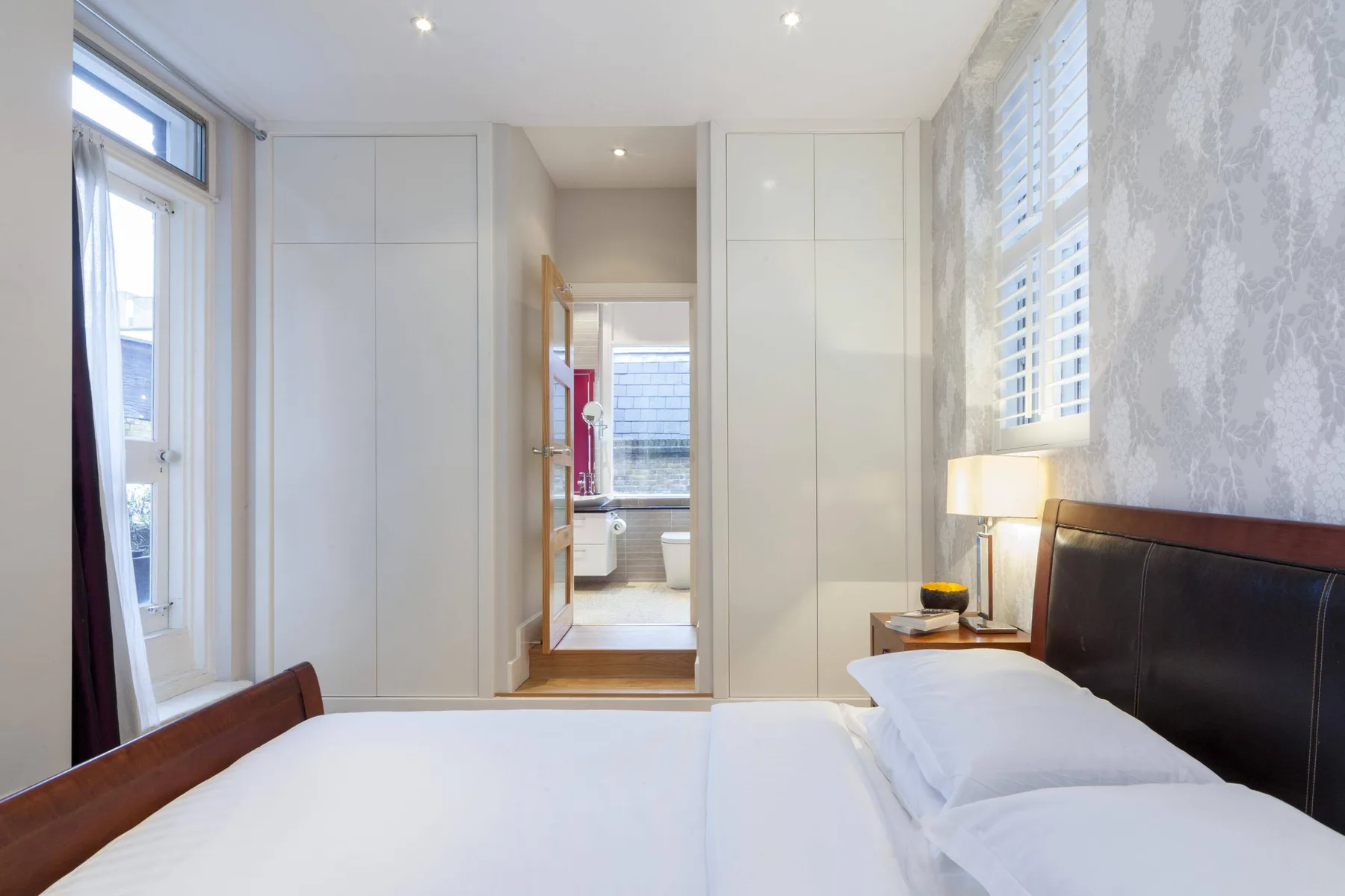 A bright bedroom with a large bed and built-in wardrobes.