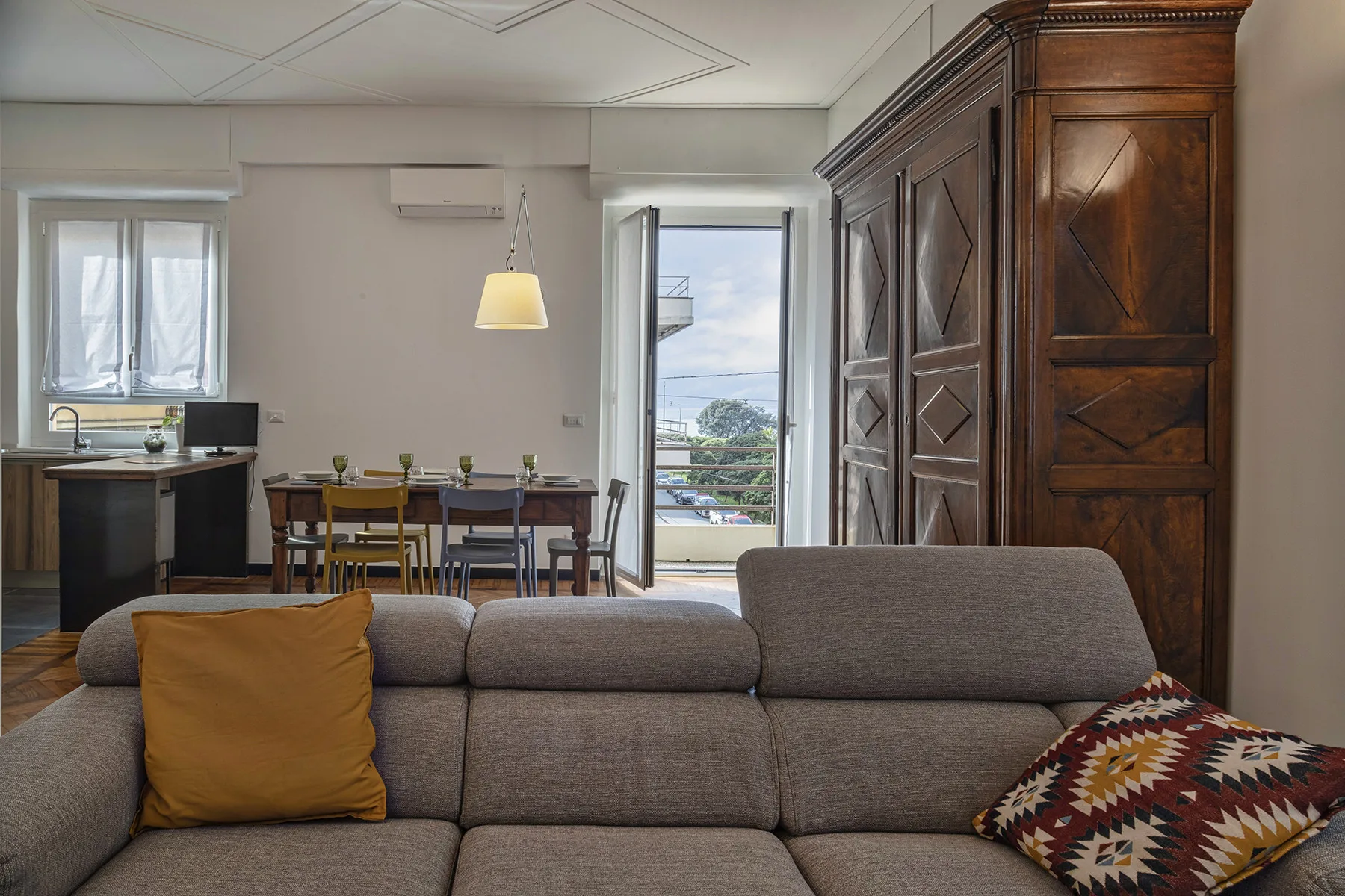 A living room with a gray sofa, patterned cushions, and a dining table by the window.