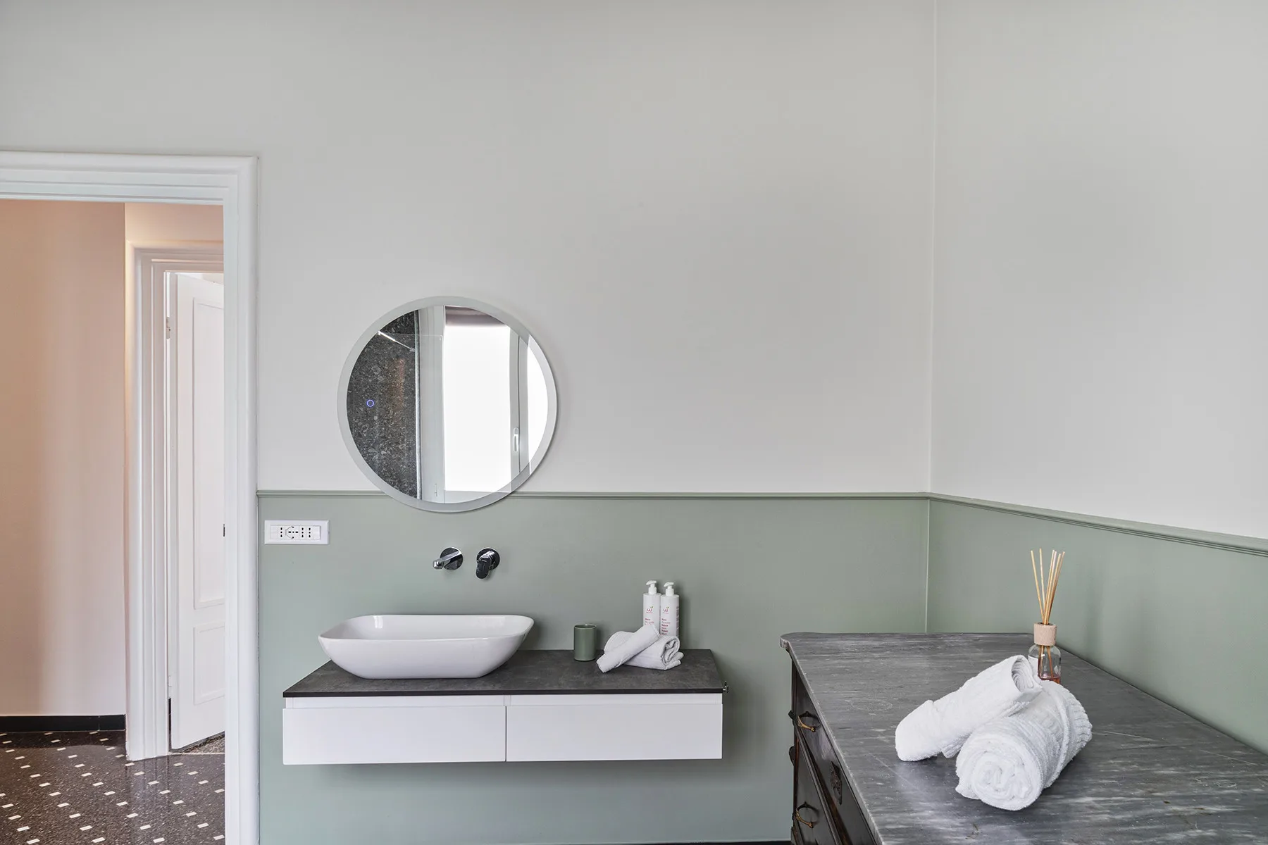 A bathroom vanity with a round mirror and neatly folded towels on the counter.