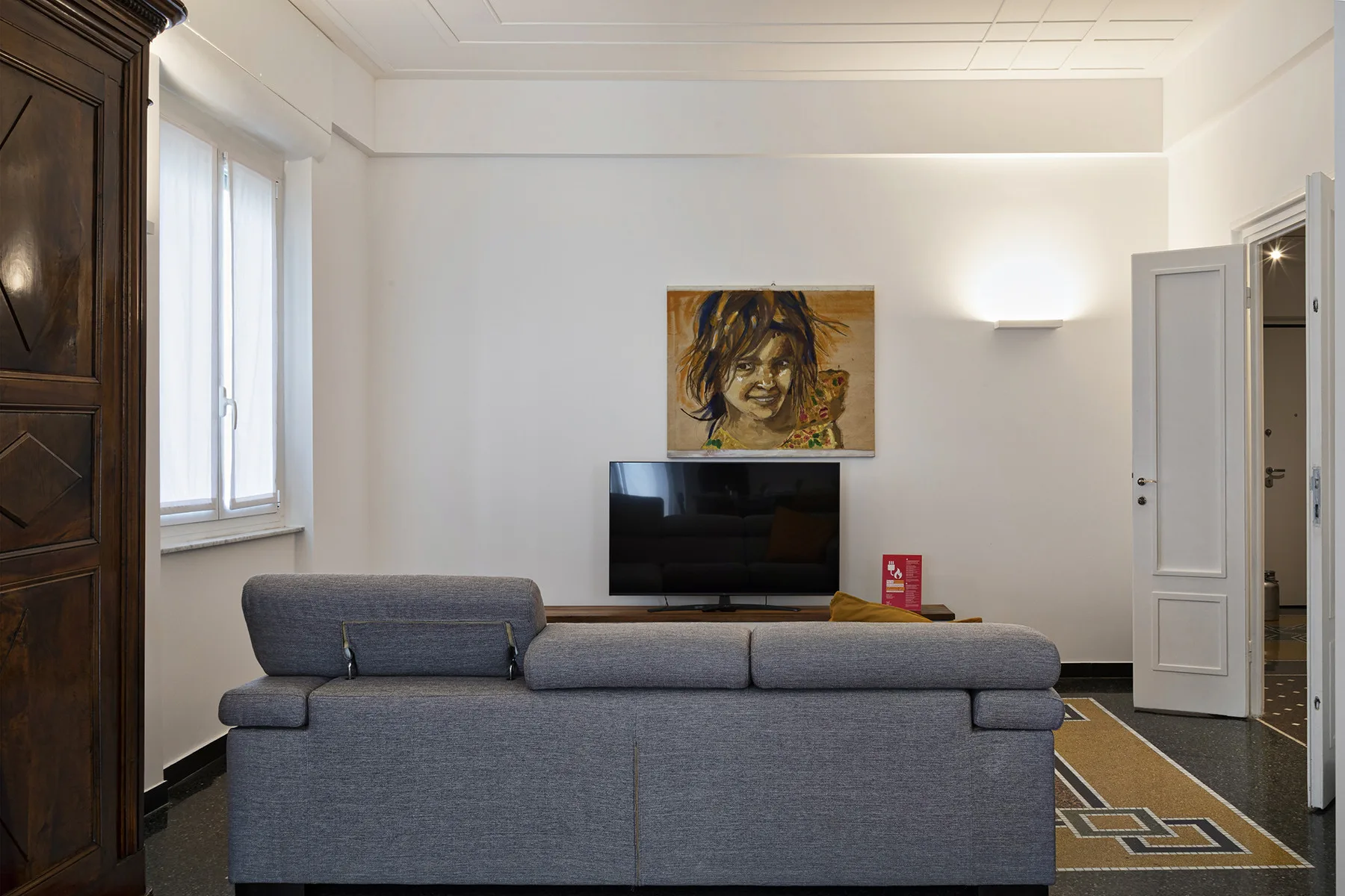 A bright living room with gray seating, a television, and a painting on the wall.
