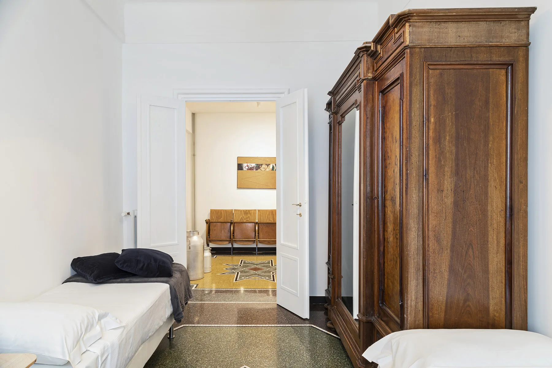 A bedroom with beds and a large wooden wardrobe beside an open doorway.