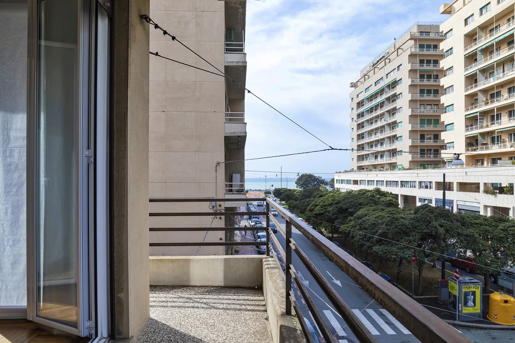 A balcony overlooks a tree-lined street and apartment buildings.