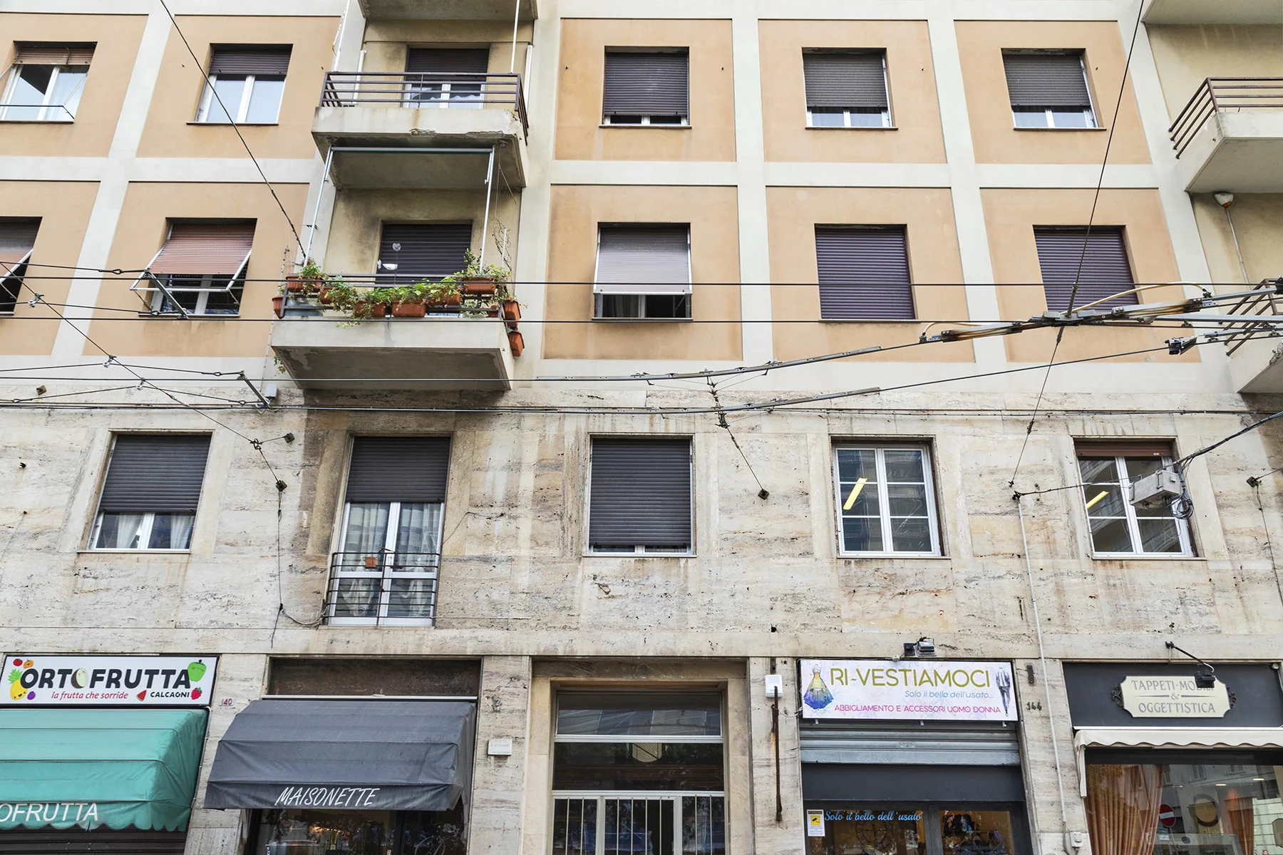A street-facing building facade with rows of windows, balconies, and ground-floor shops.