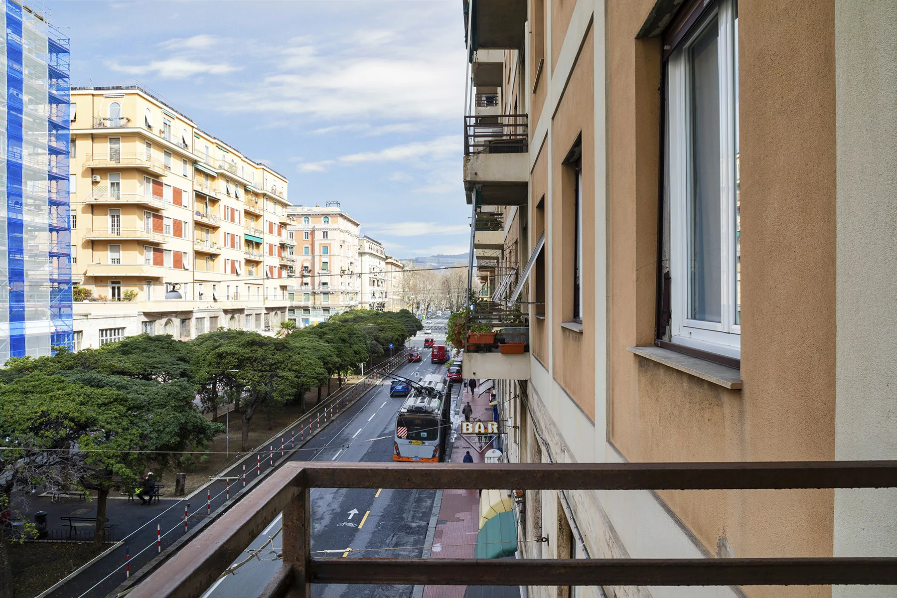 A balcony overlooks a city street lined with apartment buildings and trees.