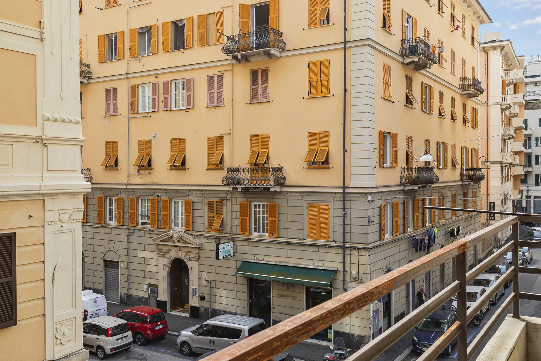 A street view of a multi-story building with balconies and shuttered windows.