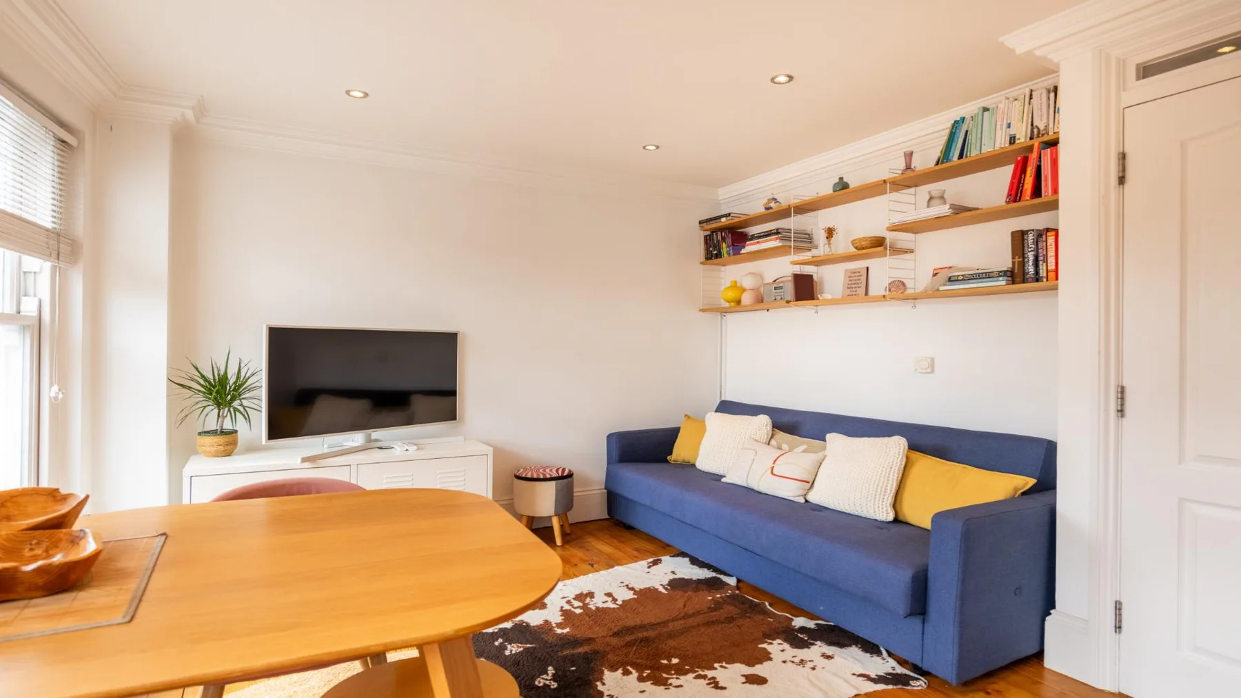 A living room with a blue sofa, wooden table, and wall shelves.