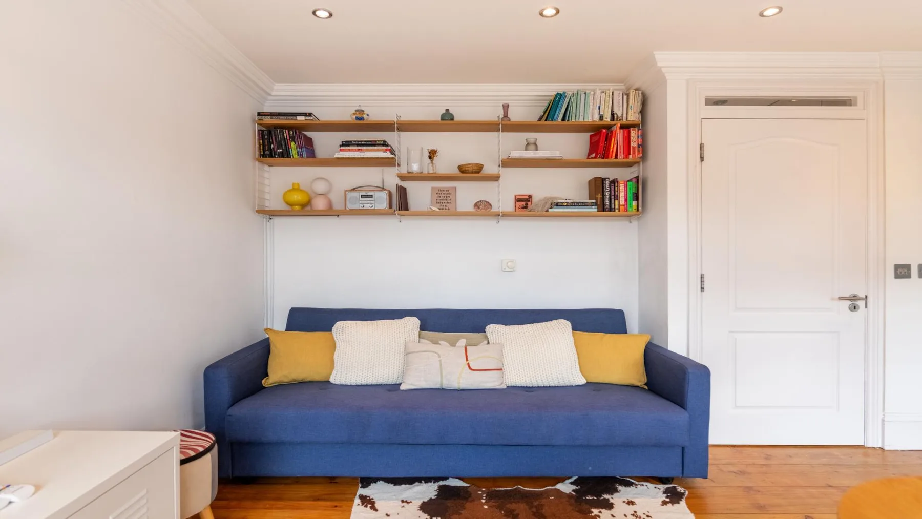 A living room with blue seating beneath wall shelves filled with books and objects.