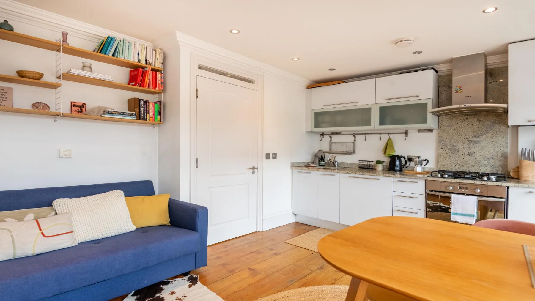 A living area with blue seating and a wooden table beside a bright kitchen.