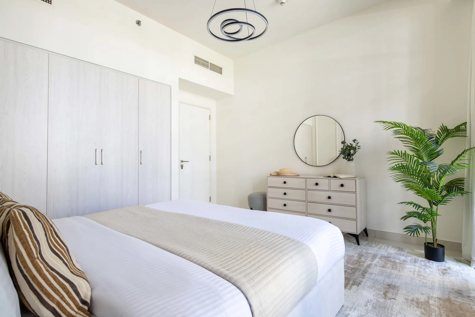 Un dormitorio luminoso con cama, armario, cómoda y una planta en maceta.