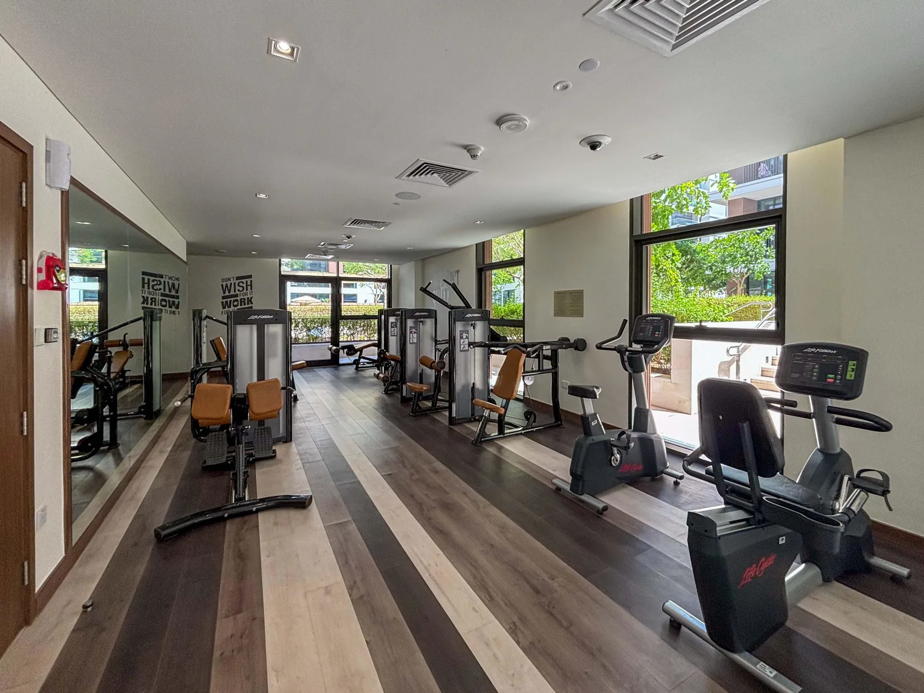 Una sala de ejercicios con máquinas junto a grandes ventanas.