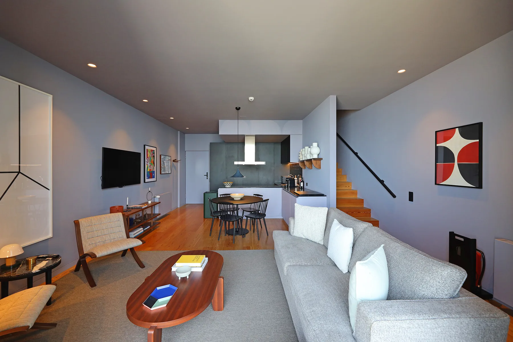 A modern living and dining area with a gray sofa and wooden staircase.
