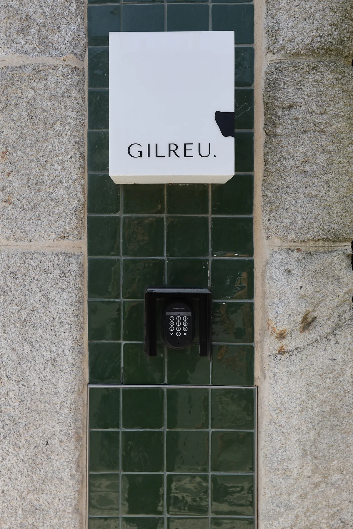 A dark green tiled wall with a white sign and keypad.