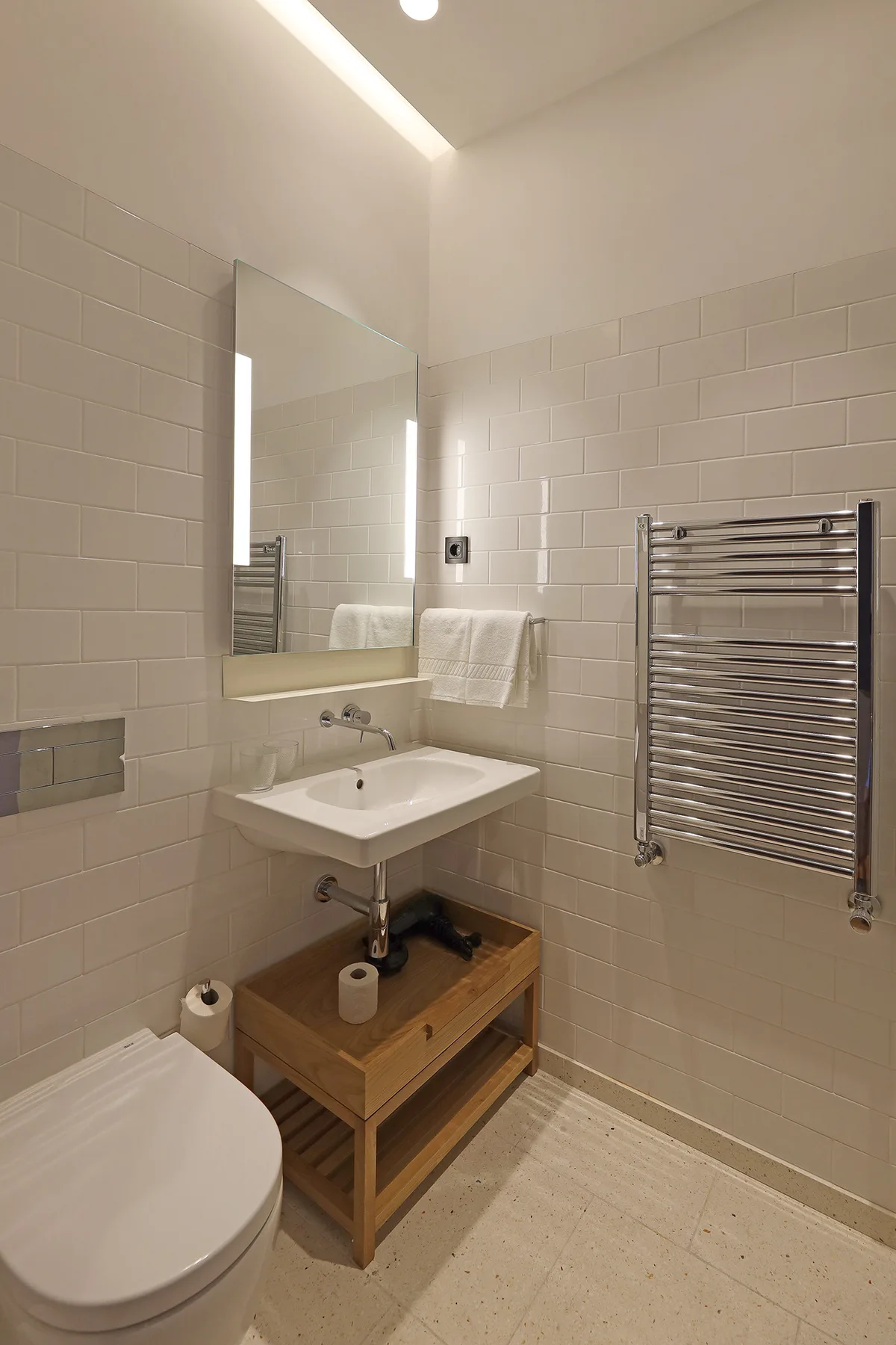 A tiled bathroom with a sink, mirror, toilet, and wall-mounted towel warmer.