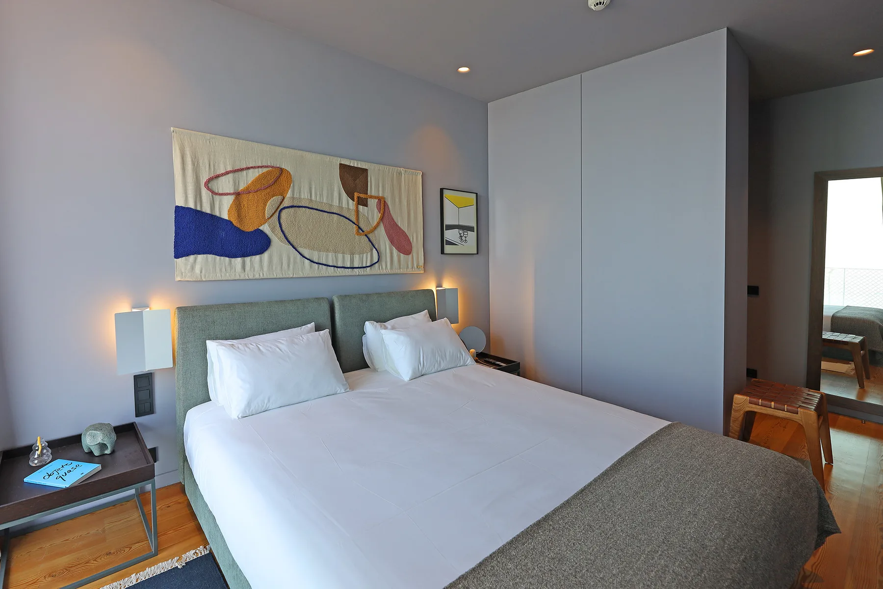 A bedroom with a neatly made bed and colorful abstract artwork above the headboard.