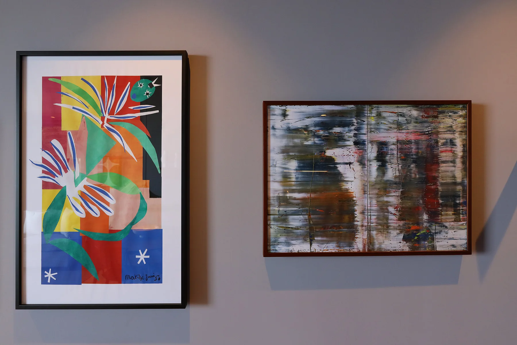 Two colorful abstract artworks hang on a gray wall.