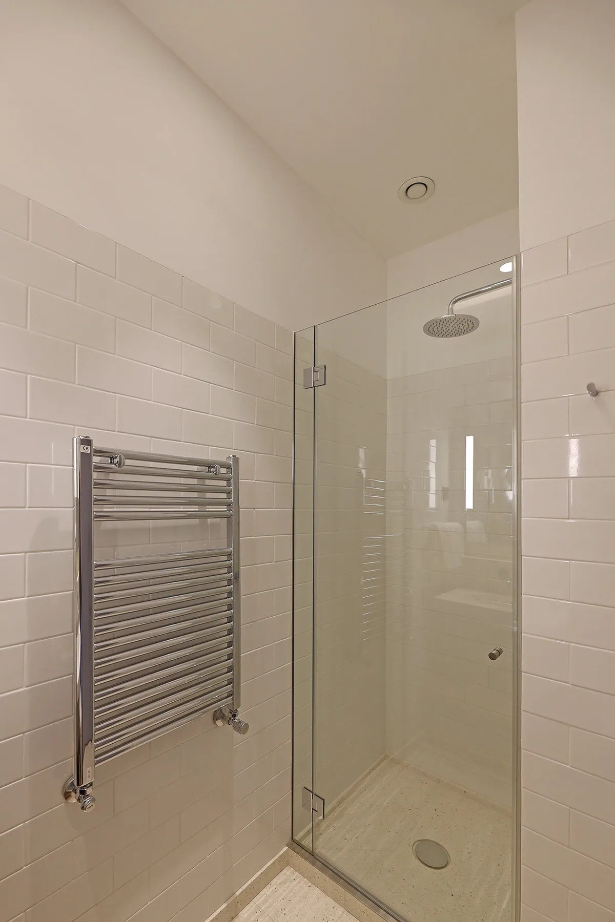 A tiled bathroom with a glass shower and a wall-mounted towel warmer.