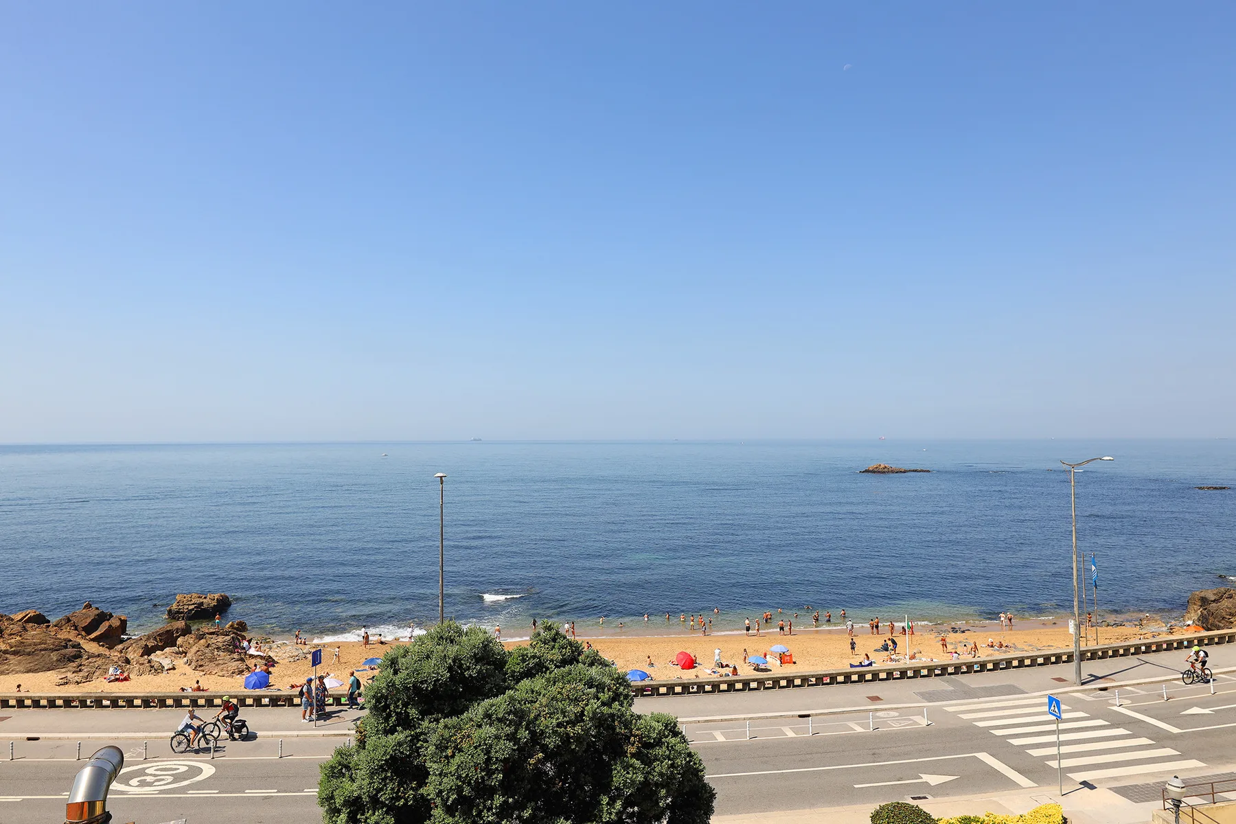 A beach and calm sea lie beyond a coastal road under a clear sky.