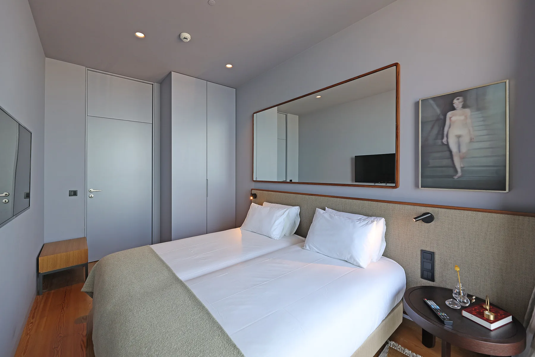 A bedroom with a double bed, a wall mirror, and framed artwork.