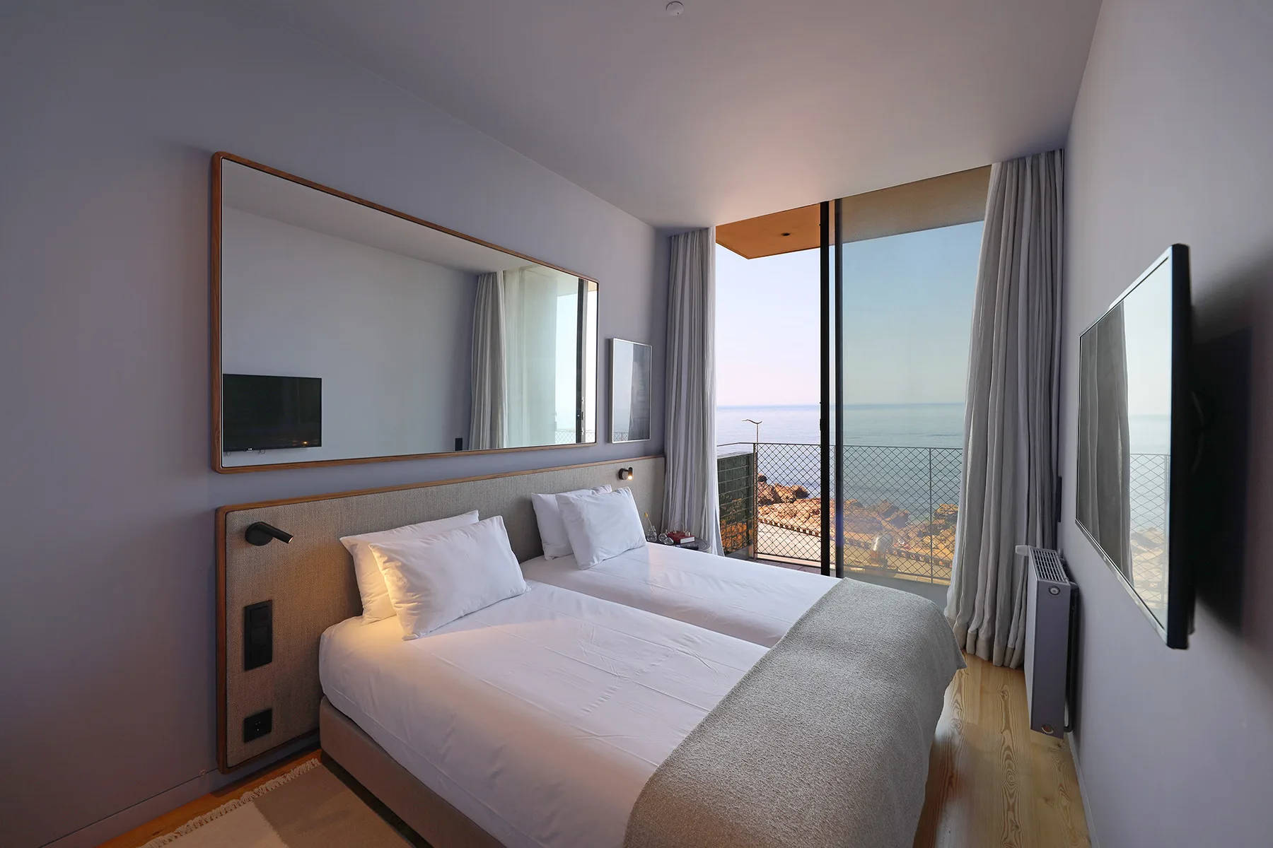 A bright bedroom with a bed beside a glass door overlooking the sea.