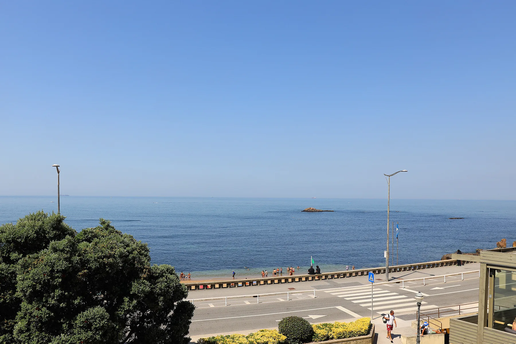 A coastal road runs beside the sea under a clear blue sky.