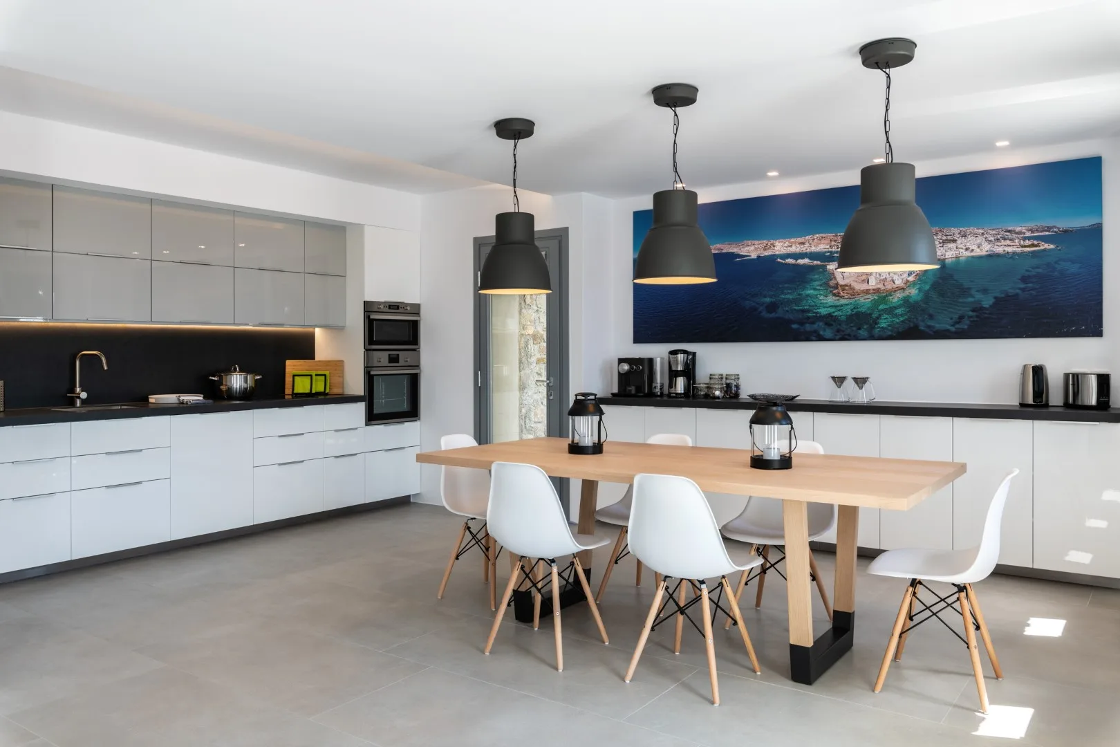 A modern kitchen and dining area with a wooden table and pendant lights.